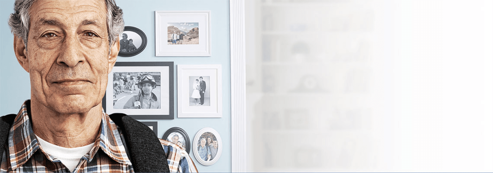 Older man stands in front of blue wall with framed pictures on it.