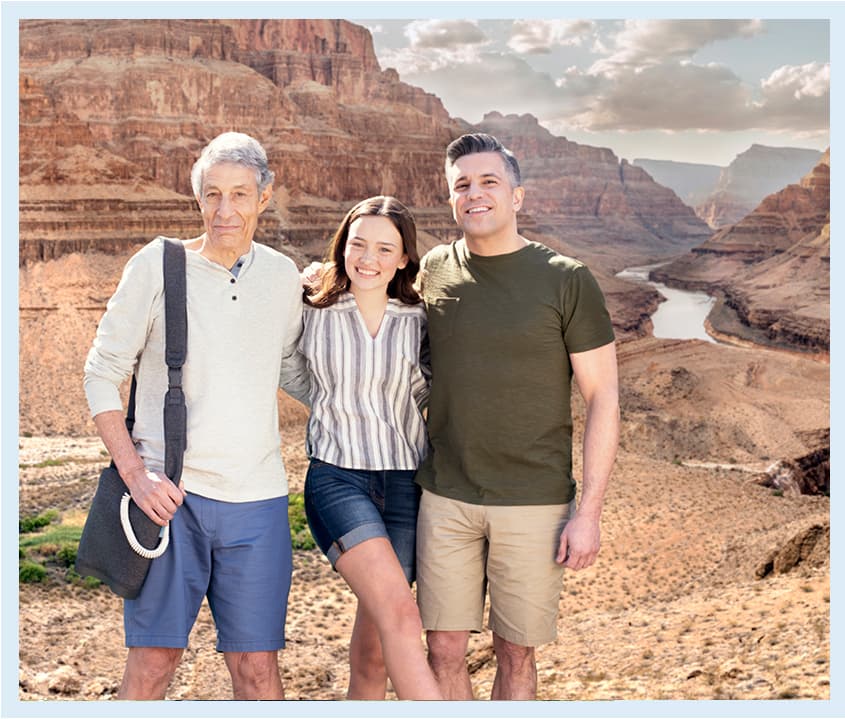 An older man with Optune Lua stands in front of a desert canyon with a younger woman and man.